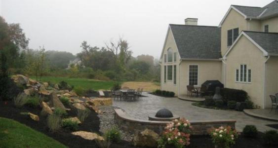 A large patio in Malvern with a sitting wall, firepit and a waterfall.