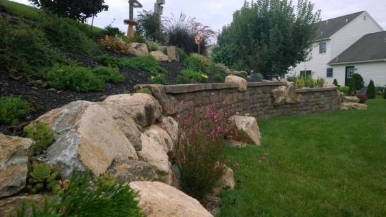 A steep slope in Douglasville with a retaining wall and boulders placed strategically on bank..