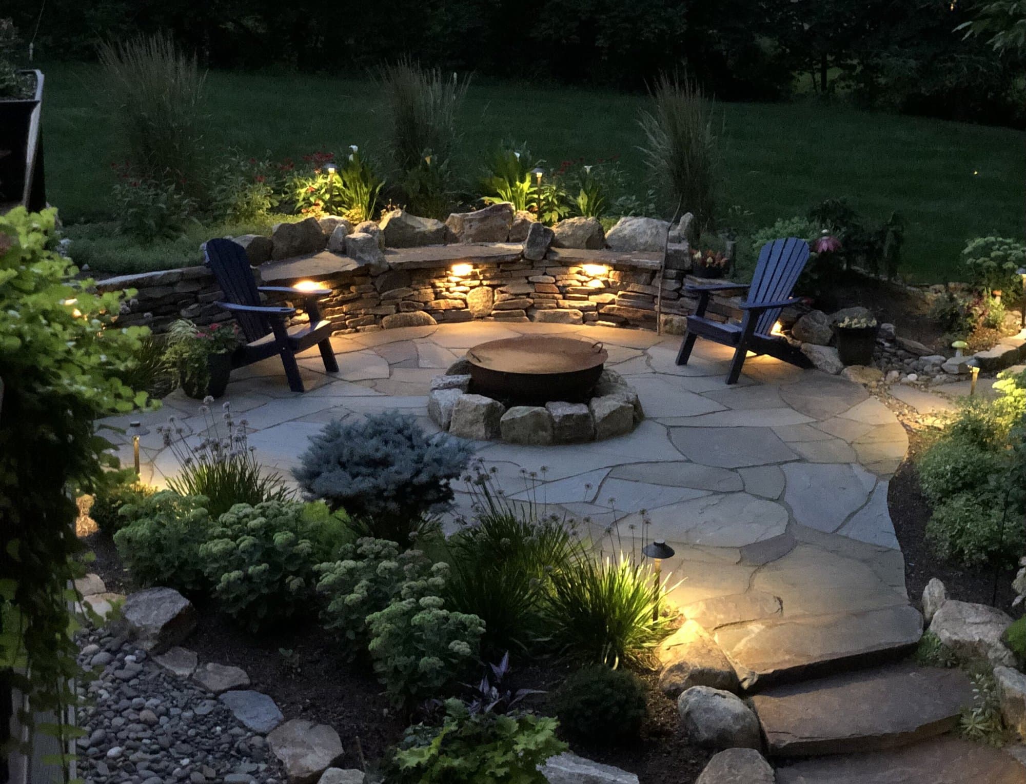 A beautiful, inviting outdoor living space in Pottstown, PA with flagstone patio, sitting wall, outdoor lighting and landscaping.